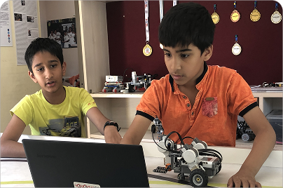 Two teenage students programming a robot on a laptop